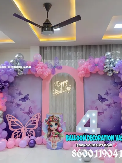 A stunning butterfly theme for a 4th birthday. The setup includes a double-panel backdrop, a pink and purple balloon arch, and large illuminated fairy-light flowers.