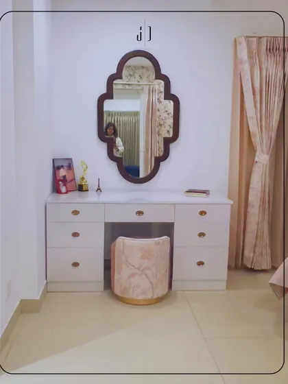 A chic and simple dressing area in a Rishikesh penthouse. The combination of a white vanity, a uniquely shaped mirror, and a plush pink stool creates a modern and feminine corner.