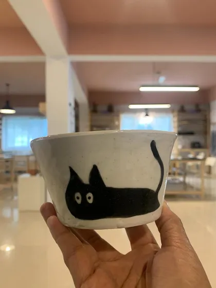 A student's creation, this quirky bowl with a hand-painted black cat, is fresh from the kiln. It's always a joy to see the unique personalities and styles that emerge from our workshops.