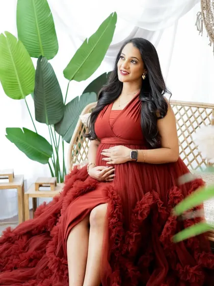 A radiant portrait of a mom-to-be in a tropical-inspired setting. Her vibrant red gown and the lush green plants create a stunning visual.