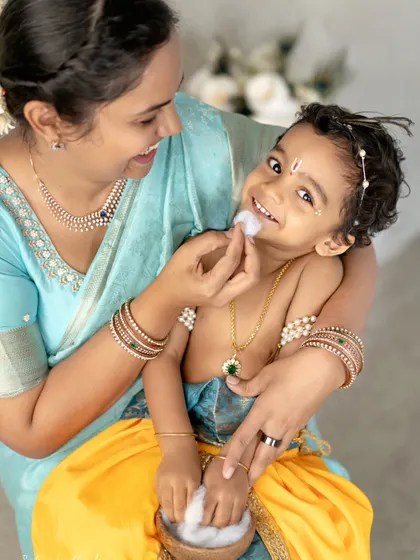 A tender moment between a mother and her son during a Krishna photoshoot. She gently wipes a bit of cotton 'butter' from his face, a sweet interaction that shows their loving bond.