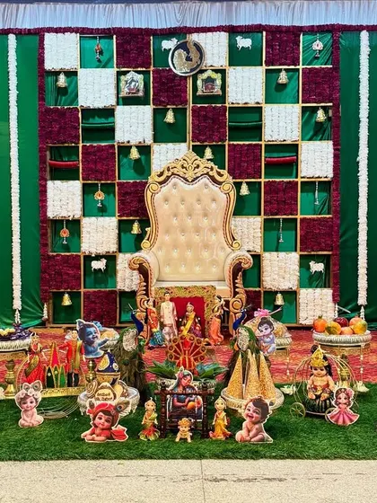 An elaborate Seemantham decoration with a unique checkered backdrop and large cow-and-calf statues. The foreground is filled with numerous dolls and decorated plates, creating a rich, festive scene.