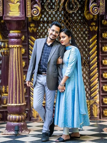 An elegant portrait of a couple on a checkered floor against an ornate golden door.