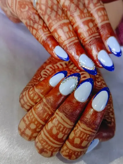 A beautiful bridal set featuring light blue nails with a dark blue French tip outline and rhinestone accents. The color provides a lovely contrast with the warm tones of the henna.