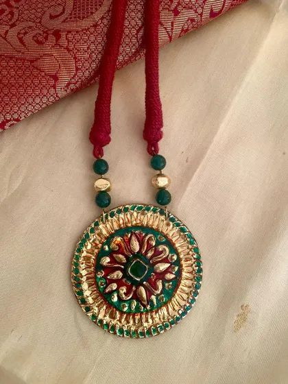 A close-up view of the detailed gesso work on a Tanjore-style pendant. The combination of red, green, and gold is a classic choice for festive occasions.