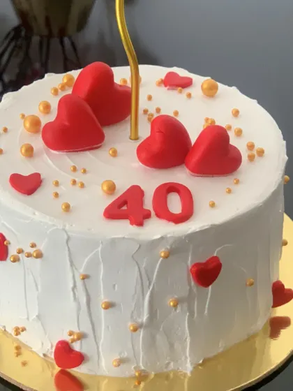 A simple and sweet cake for a 40th birthday. The white cake is decorated with red hearts and gold sprinkles for a touch of love and celebration.