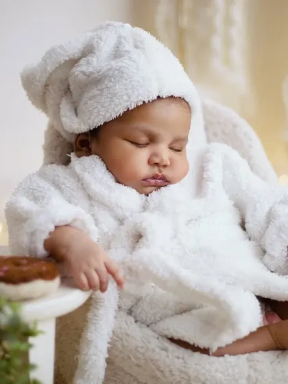 Even the tiniest babies can chill out in style. This newborn is sleeping peacefully in a fluffy white bathrobe, dreaming of coffee and donuts. This is a super cute and cozy theme for a newborn photoshoot.