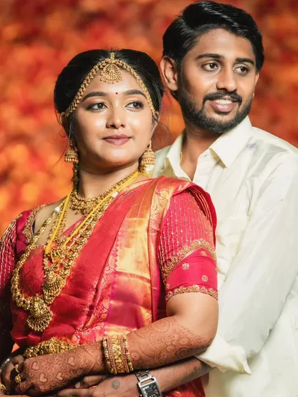 The groom stands proudly with his bride. The makeup ensures his skin is even and bright under the vibrant lights.