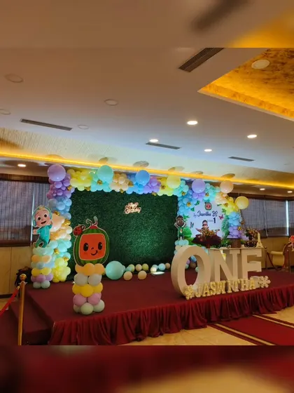 A wide shot of a Cocomelon themed stage, showing the green turf flooring and large 'ONE' letters for a first birthday.