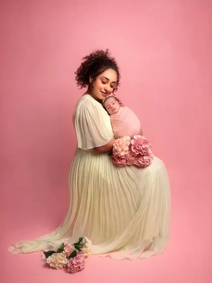 The gorgeous Pearle Maany cradling her newborn baby. The soft pastel colors of the dress and the pink background create a sweet and feminine portrait.