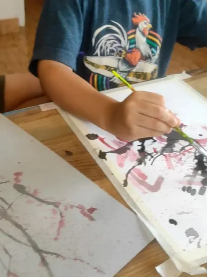 A close-up of a student using the straw painting technique to create a cherry blossom tree. This fun method teaches kids about creating textures in unexpected ways.