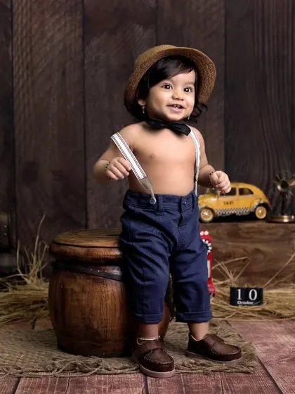 A dapper little gentleman in our vintage explorer setup. The dark wood background, antique props like a globe and lantern, and classic attire create a timeless and charming look.