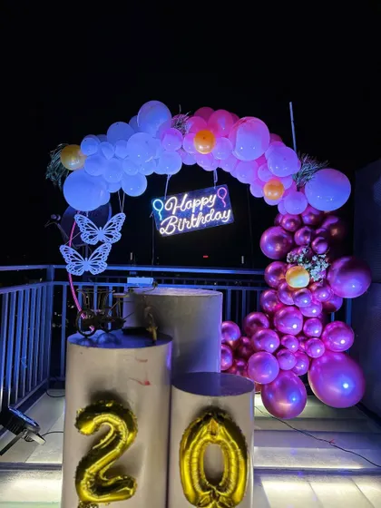 A beautiful balloon ring decoration on a rooftop at night. This setup for a 20th birthday features a purple and pink balloon arrangement, a neon sign, and butterfly accents for a magical touch.
