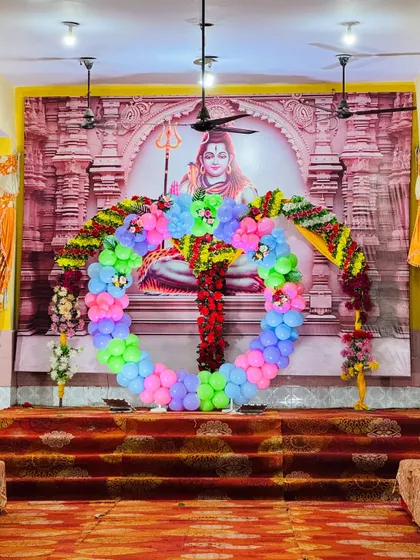 A wide shot of the Namkaran ceremony setup in a hall. The large balloon ring is placed in front of a religious backdrop, suitable for the puja.