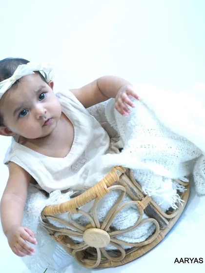 A high-angle shot of a baby sitting in a decorative woven basket, looking directly at the camera. This pose is great for capturing a baby's developing personality and curious gaze.