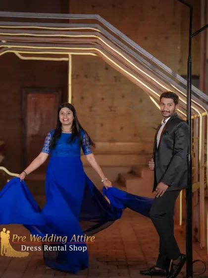 A couple posing in our royal blue trail gown and a sharp black suit. The flowing fabric of the gown adds a dynamic element, while the classic suit provides a strong, stable anchor in the photo.