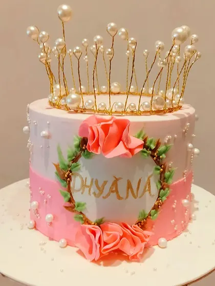 A beautiful princess-themed cake with a delicate pearl and wire crown. The hand-painted name and floral details make this a truly special cake for Dhyana.
