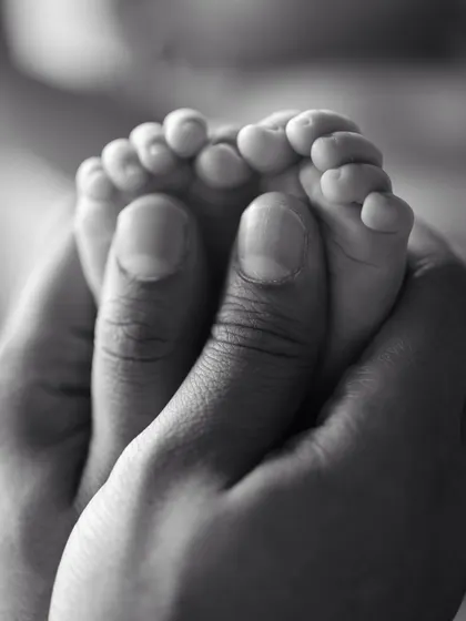 A powerful black and white macro shot of a parent's thumbs cradling their baby's feet.
