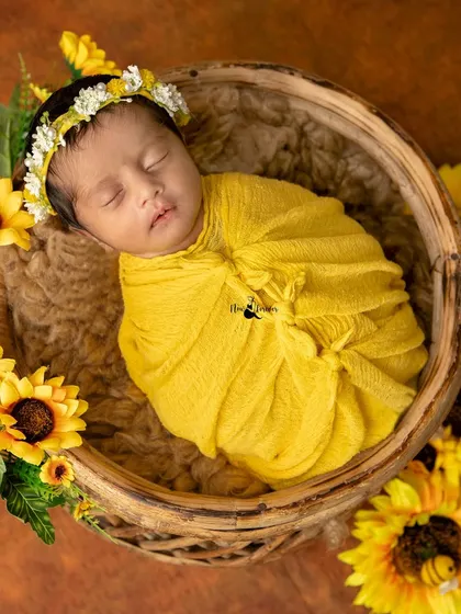 A top down view of a newborn wrapped snugly in a basket, surrounded by a ring of sunflowers. This composition creates a beautiful, artistic portrait.