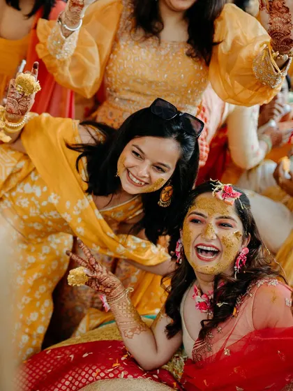 The bride and her friends share a laugh, their faces and hands covered in turmeric, a testament to a fun and memorable Haldi.