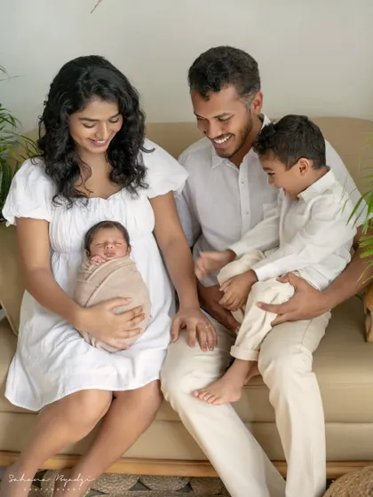 A happy family of four, relaxed and smiling on the couch. The older brother is full of energy while the parents gently hold the swaddled newborn, a perfect blend of calm and chaos.