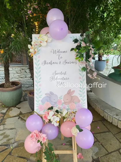 A charming welcome sign for a twins' baby shower, featuring sleeping bunnies and decorated with pastel balloons and flowers.