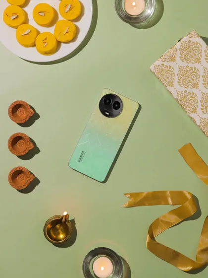 A creative flatlay with the Narzo phone, diyas, and gift wrapping elements, using a soft green background.