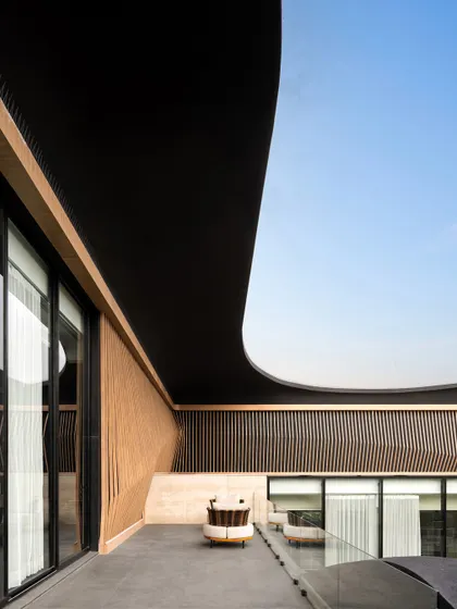 The sculpted, curving roofline of Residence Ondra creates a sheltered and intimate balcony space. This detail showcases our use of fluid forms to craft unique architectural experiences, blending wood, glass, and concrete.