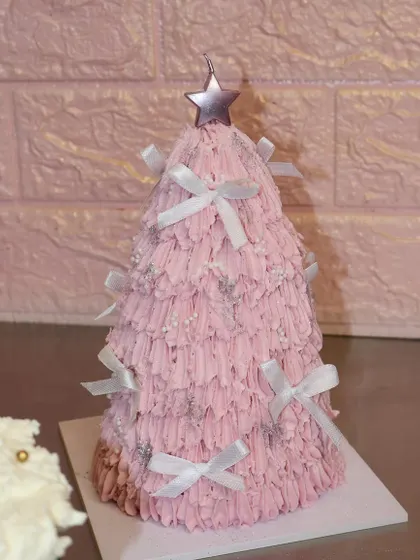 A very merry pink Christmas tree cake! This fun and festive creation is covered in textured pink frosting, sparkly details, and tiny white bows, perfect for a playful holiday celebration.