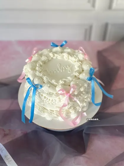 A beautiful all-white vintage cake decorated with delicate blue and pink ribbons. This design is perfect for a baby shower or a gender reveal party, offering a classic and timeless aesthetic.