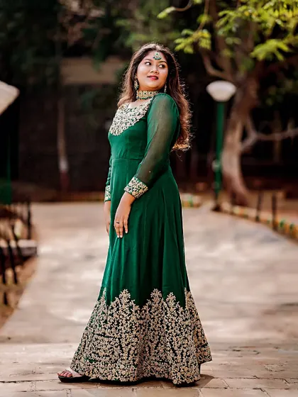 A classic portrait pose in a park setting, highlighting the rich color and detailed golden embroidery of the traditional gown.