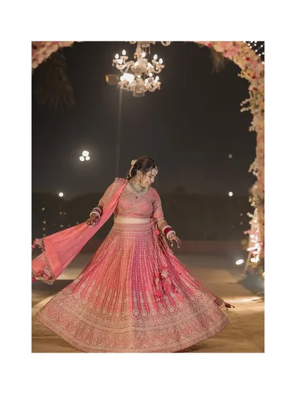 A lovely shot of the bride twirling in her pink lehenga at her nighttime wedding, with a chandelier creating a magical bokeh effect.