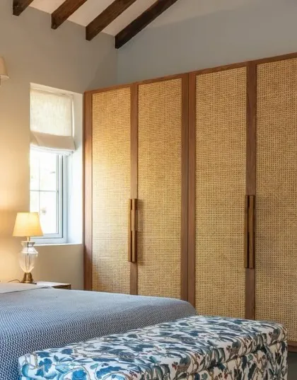 The custom wardrobe in the Goa villa bedroom features rattan paneling and sleek wooden handles, blending seamlessly with the room's rustic and coastal aesthetic.