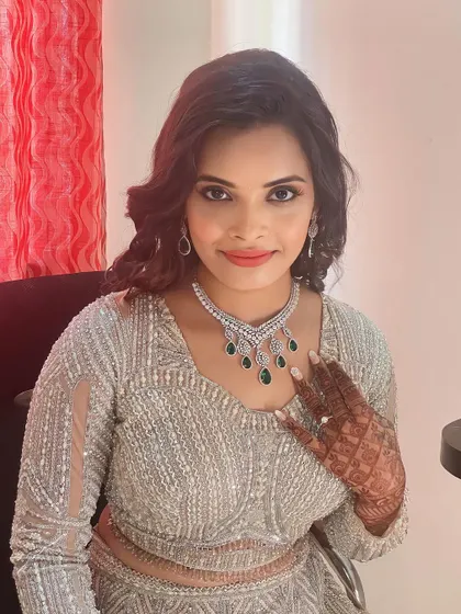 A glamorous reception look. The makeup features a defined eye and a neutral lip, allowing the sparkling diamond and emerald necklace to take center stage.