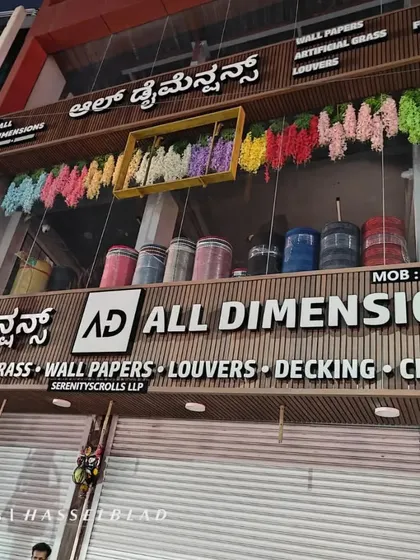 A night view of my well-lit store, showcasing the brand and the range of services I provide: flooring, artificial grass, wallpapers, louvers, decking, and cladding.