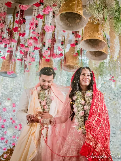 A joyful shot of the couple during their pheras. They are smiling and looking up at the beautiful floral and bell decorations of the mandap.