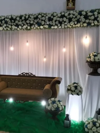 A simple yet elegant reception stage with white floral arrangements, hanging Edison bulbs, and a classic sofa, perfect for intimate gatherings.