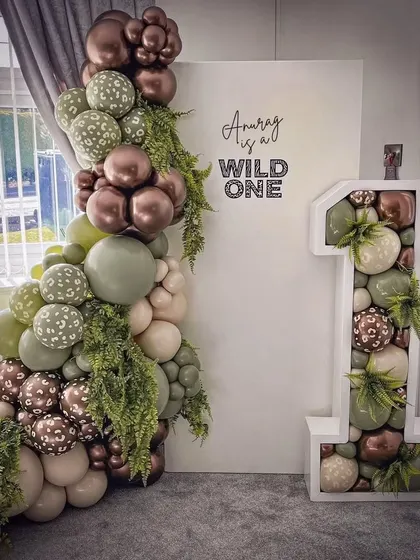 "Anurag is a Wild One." This jungle-themed setup for a first birthday uses a sophisticated palette of olive green and brown, with animal-print balloons and a large mosaic number "1".