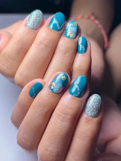 A beautiful teal and silver set, combining a solid glitter nail with a marble effect and gold foil accents.