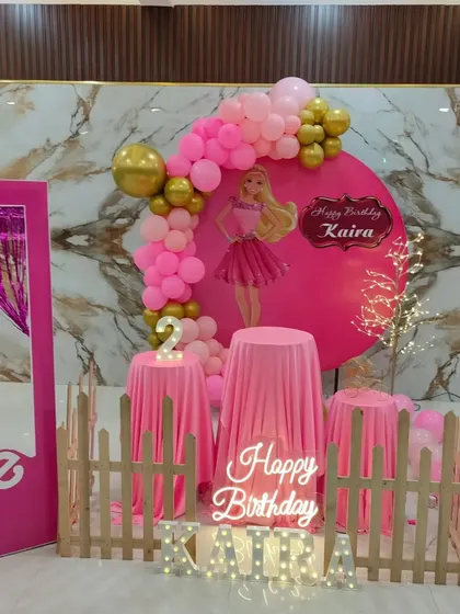 A Barbie-themed second birthday party with a life-size photo box and a pink circular backdrop against a marble wall.