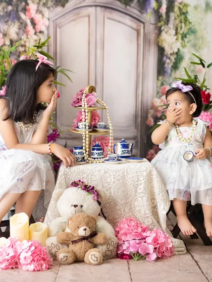 Sisters sharing secrets during a floral tea party. Sibling photoshoots are designed to be fun and interactive, capturing their unique friendship.
