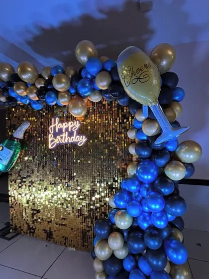 This setup with a gold shimmer wall, neon sign, and rich balloon colors is perfect for a lively and stylish birthday bash.