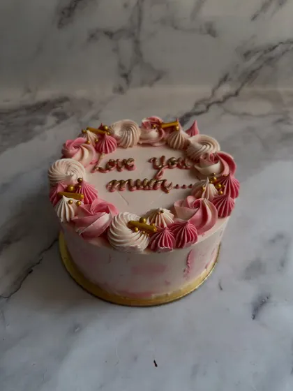 A beautiful cake for Mother's Day, featuring "Love you mum" in delicate script, surrounded by a wreath of pink and white piped meringues.