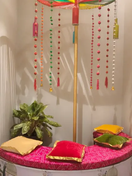 A cozy and colorful seating corner created for a Navratri event. The setup includes a large decorative umbrella, hanging ornaments, and bright cushions.