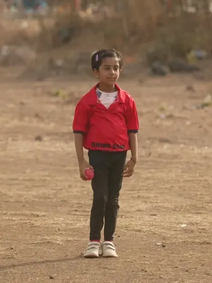 The future of women's cricket starts here. A young girl, one of our youngest players, stands ready on the field during our anniversary match.