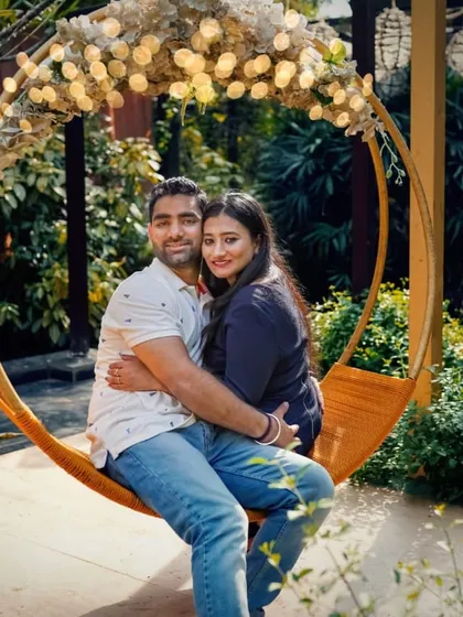 A lovely portrait of a couple seated on a circular swing decorated with lights, a popular setup for pre-wedding photoshoots.