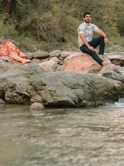 A full shot of the couple in a relaxed pose by the river, highlighting the beautiful natural location of their pre-wedding photography session.