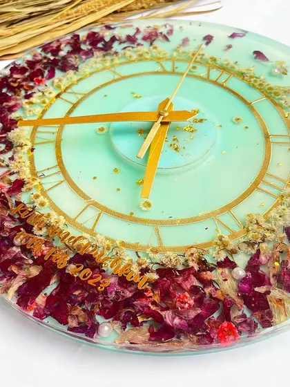 This 12-inch wall clock features preserved orchids against a light sea-green background. The purple and white flowers are complemented by delicate gold flakes.