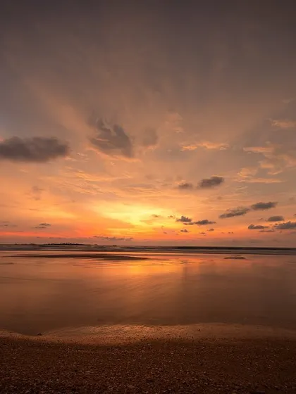 A wide, vibrant sunset over the ocean, with the light reflecting on the wet sand. This image is all about the incredible colors that nature can produce.