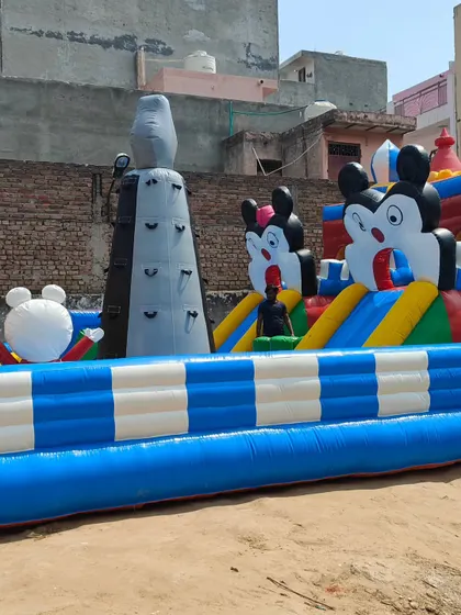 A side view of the Mickey-themed "Fun City" bouncy, showing the inflatable climbing tower and multiple character figures that decorate the structure.